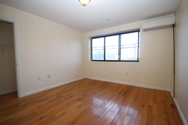 unfurnished bedroom with a closet, baseboards, light wood-style floors, and a wall mounted AC