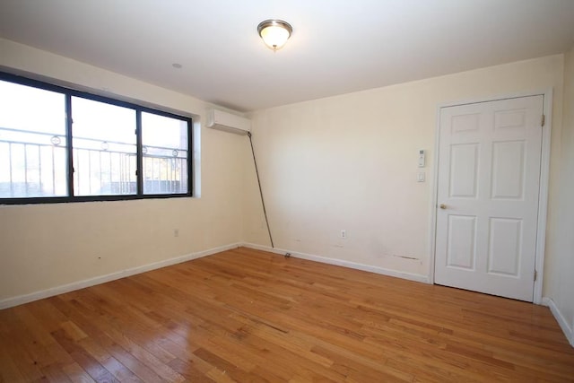 empty room featuring a wall unit AC, light wood-style flooring, and baseboards