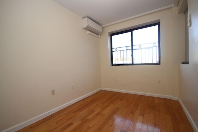 spare room featuring light wood-style flooring, an AC wall unit, and baseboards