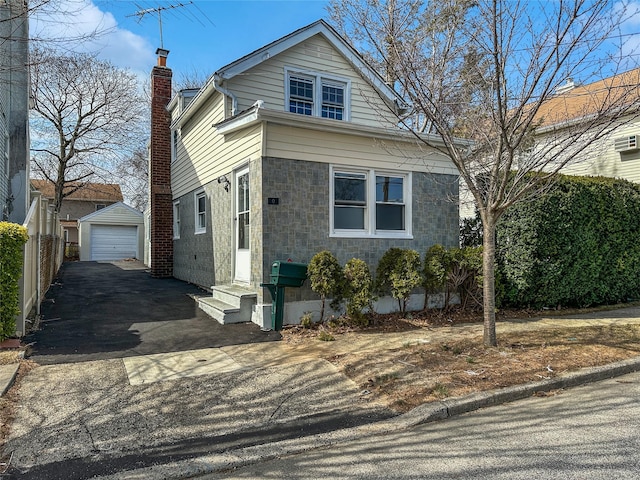 view of front of house featuring aphalt driveway, entry steps, a chimney, a garage, and an outdoor structure