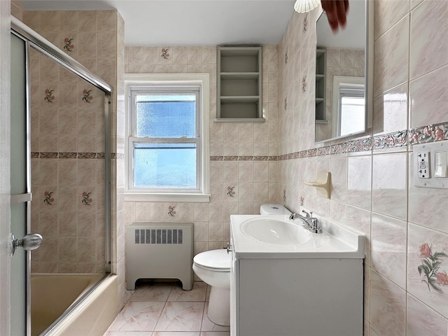 bathroom with vanity, shower / bath combination with glass door, radiator heating unit, tile walls, and toilet