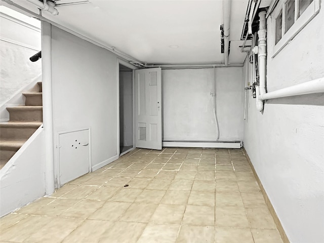 finished basement featuring a baseboard radiator, baseboards, and stairway