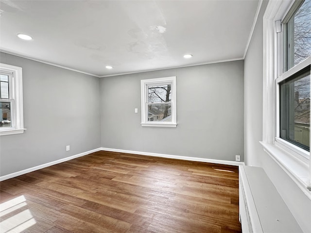 spare room featuring plenty of natural light, crown molding, baseboards, and wood finished floors