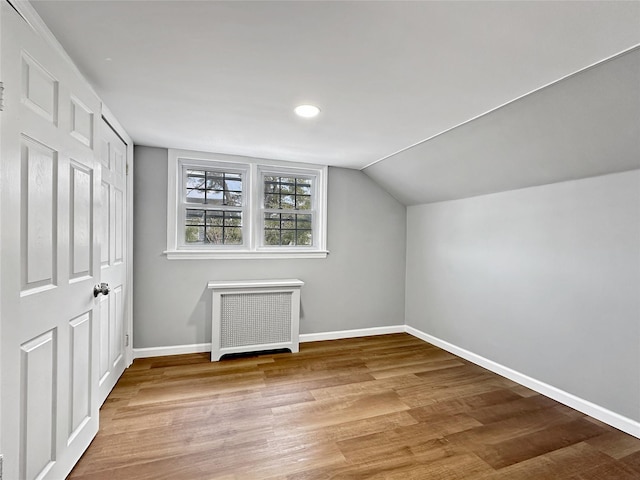 bonus room featuring baseboards, radiator, wood finished floors, and vaulted ceiling