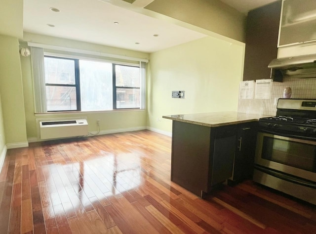 kitchen featuring dark cabinetry, wood finished floors, gas stove, a wall mounted AC, and tasteful backsplash