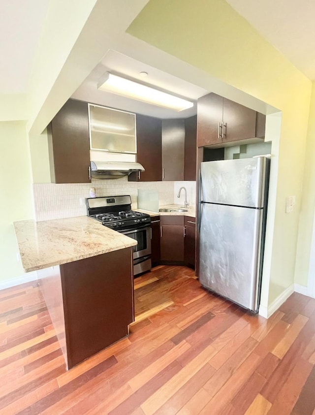 kitchen featuring light wood-type flooring, a sink, backsplash, stainless steel appliances, and a peninsula