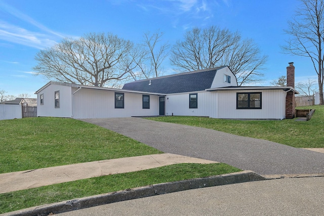 view of front of property with fence, driveway, a gambrel roof, a chimney, and a front lawn