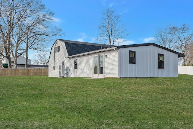 rear view of house featuring a gambrel roof, roof with shingles, a yard, and fence