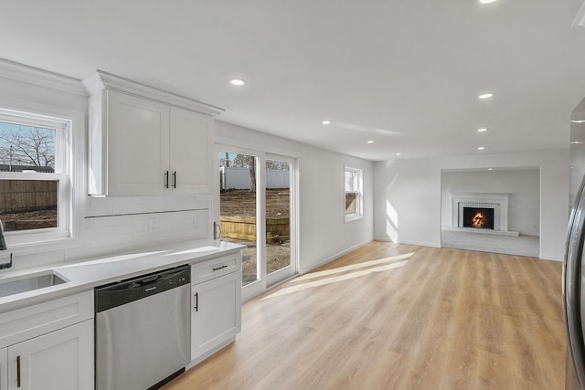 kitchen featuring light wood finished floors, backsplash, stainless steel dishwasher, white cabinetry, and light countertops