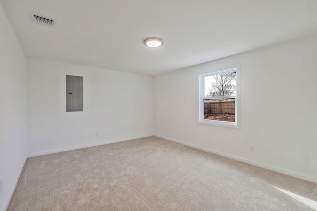 spare room featuring electric panel, light colored carpet, visible vents, and baseboards