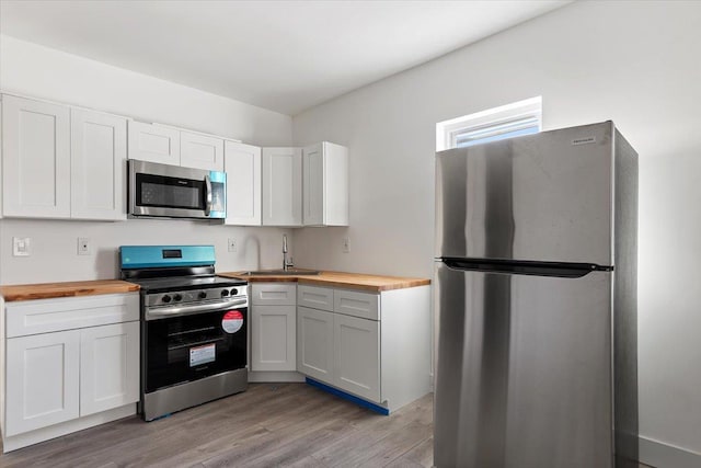 kitchen with white cabinets, appliances with stainless steel finishes, wood counters, and light wood-style floors