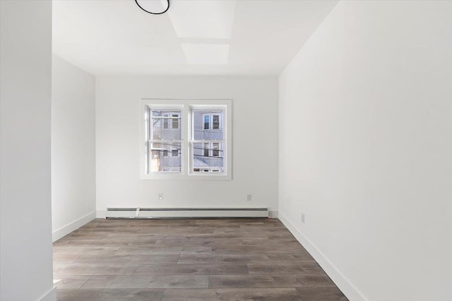 unfurnished room featuring a baseboard heating unit, baseboards, and wood finished floors