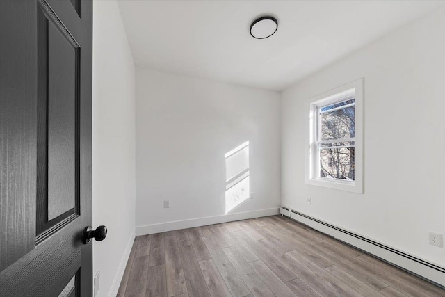 empty room with a wealth of natural light, a baseboard heating unit, baseboards, and wood finished floors