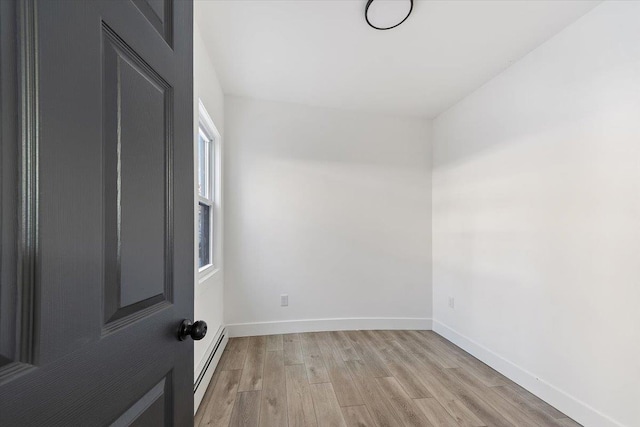 unfurnished room featuring light wood-style flooring, a baseboard heating unit, and baseboards