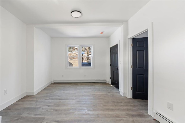 empty room featuring a baseboard heating unit, wood finished floors, baseboards, and baseboard heating