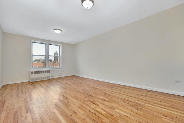 unfurnished room featuring radiator, baseboards, and light wood finished floors