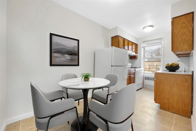 kitchen featuring under cabinet range hood, backsplash, white appliances, brown cabinetry, and light countertops