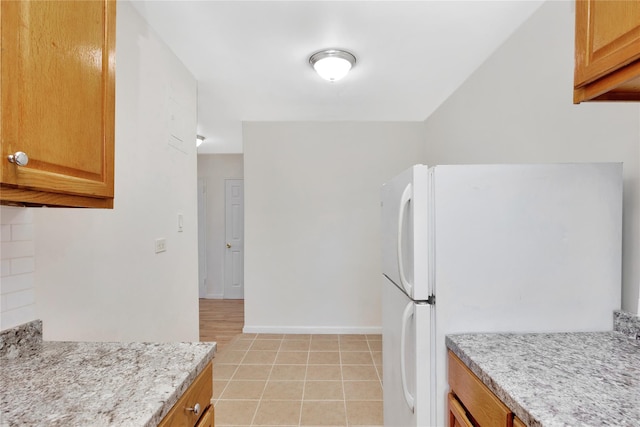 kitchen featuring light tile patterned floors, brown cabinets, freestanding refrigerator, and baseboards