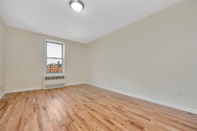 spare room featuring light wood-style floors, baseboards, and radiator