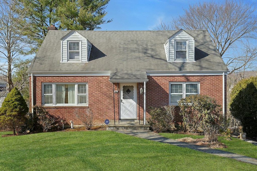 cape cod home featuring brick siding and a front yard