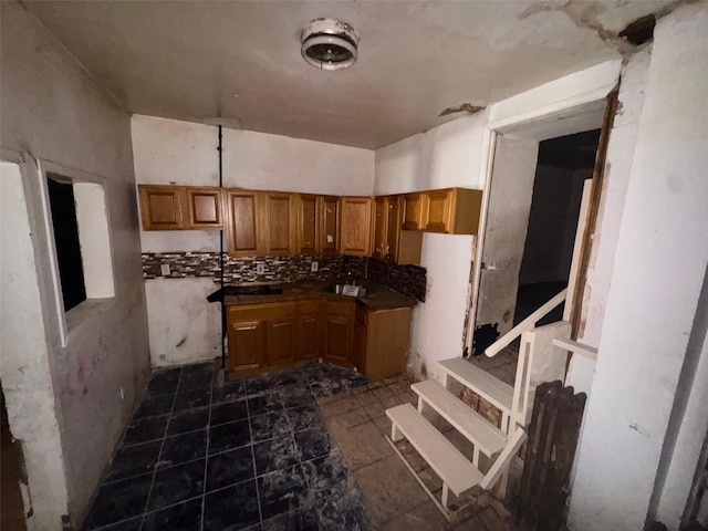 kitchen featuring a sink, brown cabinets, backsplash, and dark countertops