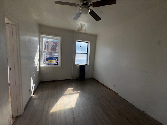 empty room with a ceiling fan, radiator, and wood finished floors