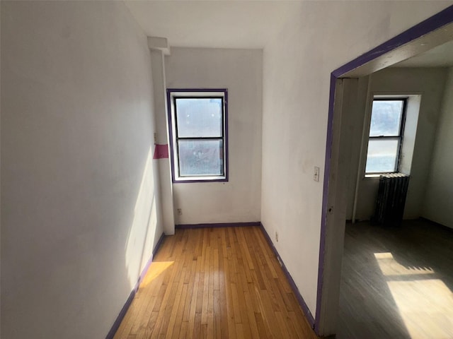 corridor with radiator heating unit, baseboards, and light wood-type flooring