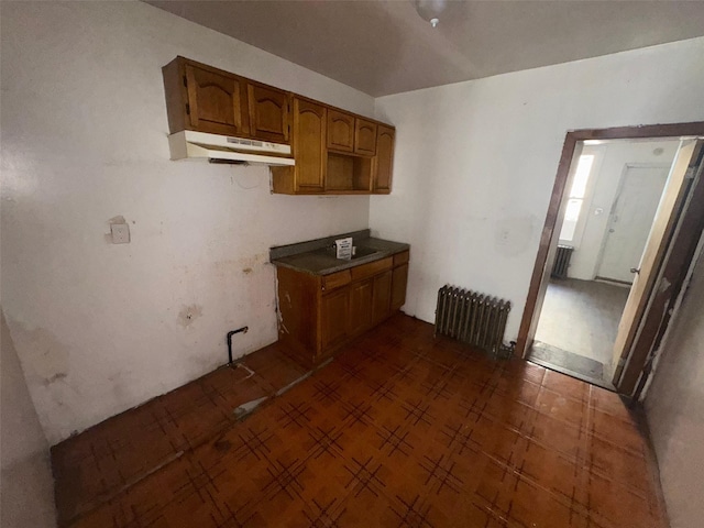 kitchen featuring under cabinet range hood, brown cabinets, and radiator heating unit