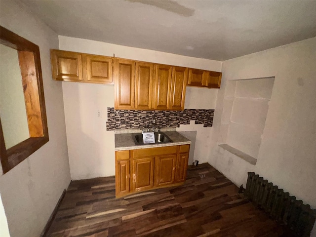 kitchen featuring brown cabinetry, dark wood-style flooring, tasteful backsplash, and a sink