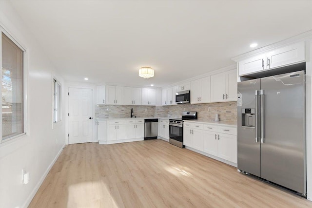 kitchen with tasteful backsplash, light wood finished floors, light countertops, appliances with stainless steel finishes, and white cabinets