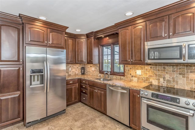 kitchen featuring backsplash, light stone counters, recessed lighting, appliances with stainless steel finishes, and a sink