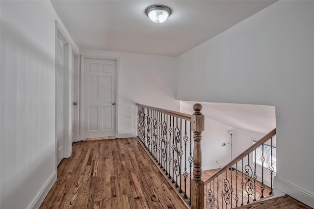 corridor with baseboards, an upstairs landing, and wood finished floors