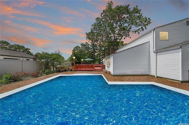 pool at dusk featuring a deck, fence, and a fenced in pool