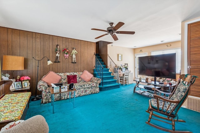 living area featuring stairway, wood walls, a ceiling fan, and carpet