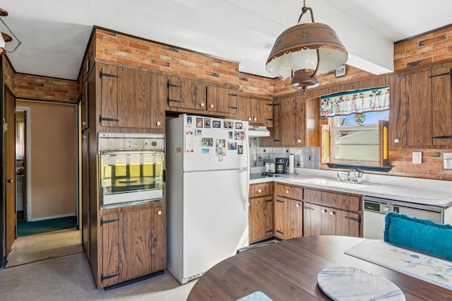 kitchen featuring a sink, under cabinet range hood, white appliances, brick wall, and light countertops