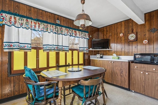 dining space featuring beam ceiling, light floors, and wood walls