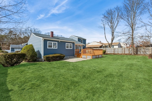 back of house featuring a chimney, a wooden deck, a yard, and fence