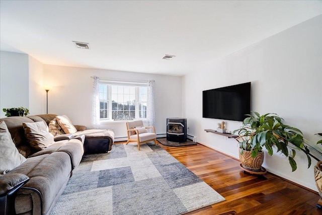 living room featuring visible vents, wood finished floors, a wood stove, and a baseboard radiator