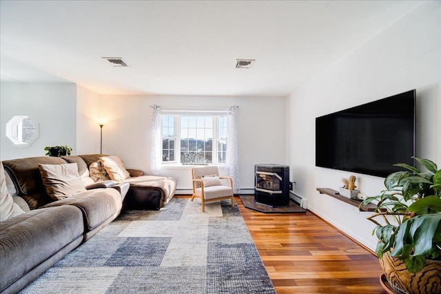 living area with visible vents, baseboard heating, wood finished floors, and a wood stove