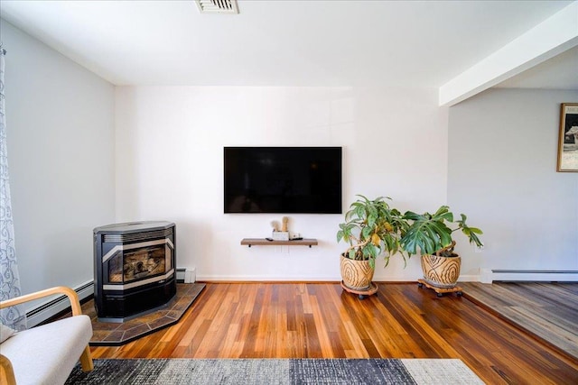 living area featuring baseboard heating, a wood stove, visible vents, and wood finished floors