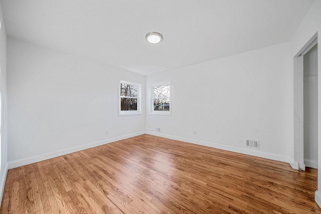 spare room featuring wood finished floors, visible vents, and baseboards