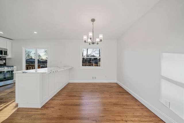 unfurnished dining area with a wealth of natural light, a notable chandelier, baseboards, and light wood finished floors