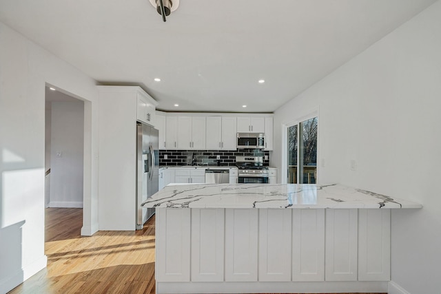 kitchen with decorative backsplash, light wood-style flooring, appliances with stainless steel finishes, a peninsula, and white cabinets