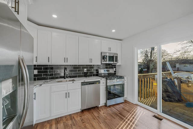 kitchen with light wood finished floors, light stone counters, decorative backsplash, appliances with stainless steel finishes, and a sink