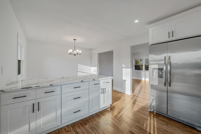 kitchen with light stone counters, wood finished floors, stainless steel fridge with ice dispenser, white cabinetry, and a notable chandelier