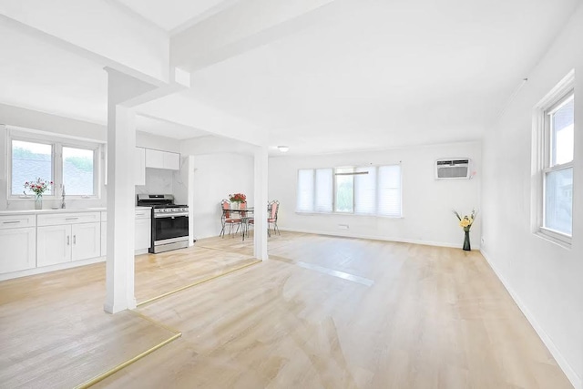 28-34 Corporal Kennedy St, Flushing, NY 11360 - unfurnished living room featuring light wood-style flooring, a wall mounted AC, a sink, and baseboards
