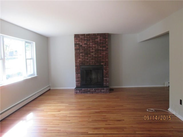 unfurnished living room featuring a baseboard heating unit, a brick fireplace, baseboards, and light wood-type flooring