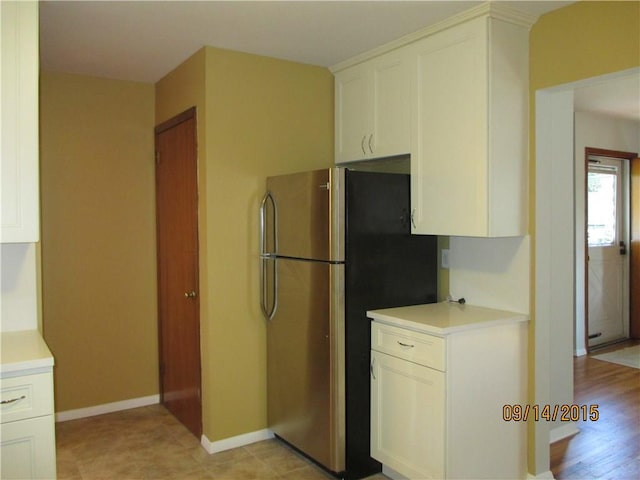 kitchen featuring baseboards, white cabinets, light countertops, and freestanding refrigerator