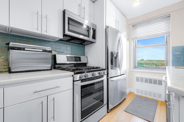 kitchen with light wood-style flooring, radiator heating unit, appliances with stainless steel finishes, white cabinets, and light countertops