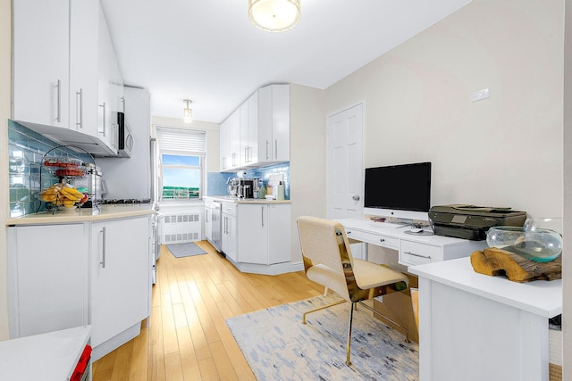 kitchen with light wood-style flooring, backsplash, stainless steel appliances, white cabinets, and light countertops